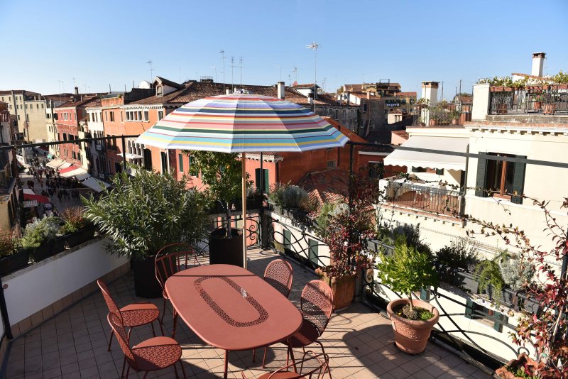 Una terrazza soleggiata con tavolo e sedie arancioni con vista su Venezia