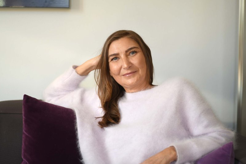 Coach Giselle è seduta su un divano nero, appoggia la testa sulla mano e guarda verso la fotocamera