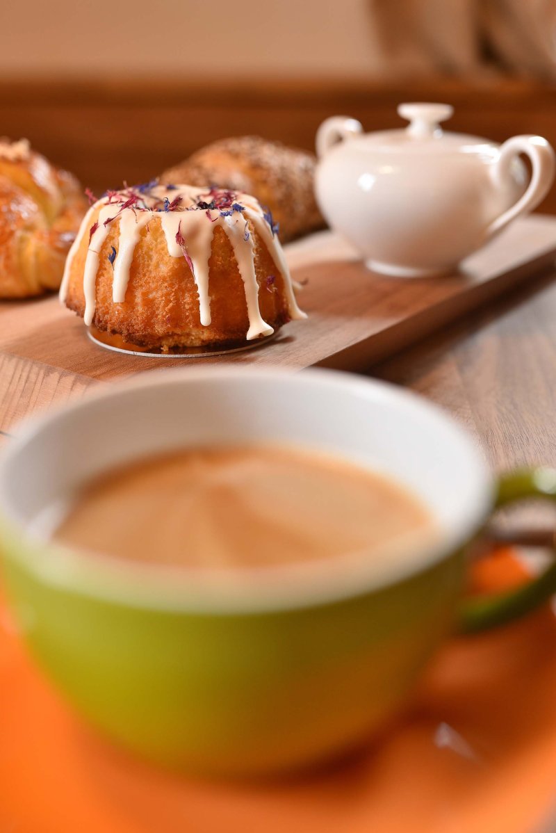 Grüne Kaffeetasse mit frisch gebrühtem Kaffee, dahinter ein kunstvoll verzierter kleiner Gugelhupf