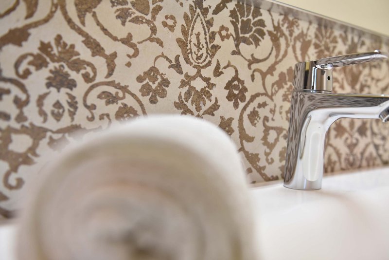 Detailaufnahme eines schön eingerollten Handtuchs im Badezimmer, im Hintergrund die kunstvolle Wand mit braun gemusterter Tapete