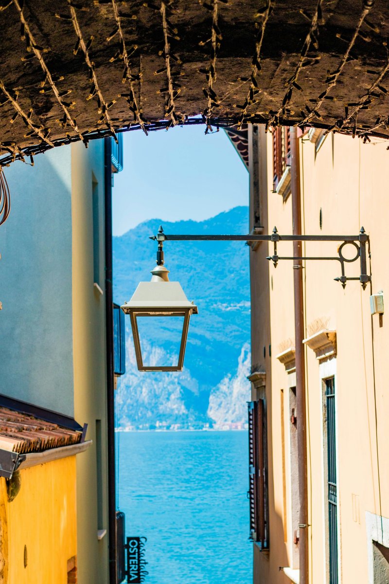 Blick durch eine schmale Gasse auf den türkisblauen Gardasee