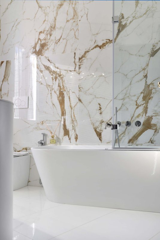 Helles Badezimmer mit weißer Badewanne und gold-marmorierter Wand im Hintergrund