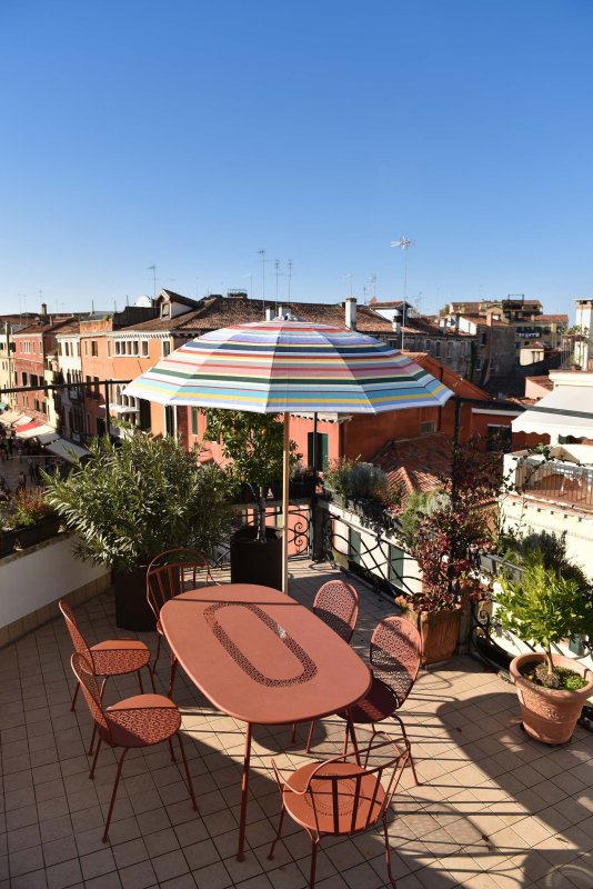 Una terrazza soleggiata con tavolo e sedie arancioni con vista su Venezia