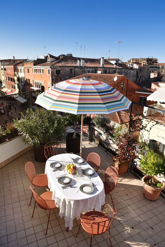 Ein gedeckter Tisch unter dem Sonnenschirm auf der Terrasse mit Blick auf Venedig