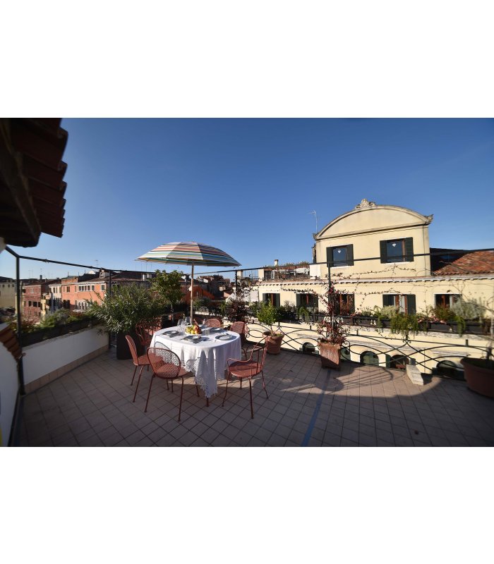 Ein Tisch mit weißer Tischdecke und Stühlen rundherum auf sonniger Terrasse