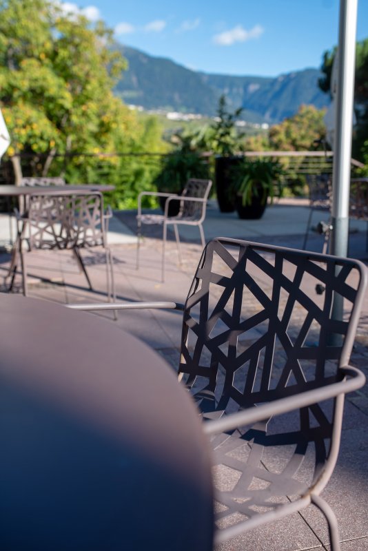Gemütliche Terrasse mit Gartenmöbeln und Palmen in Algund an einem Sommertag.