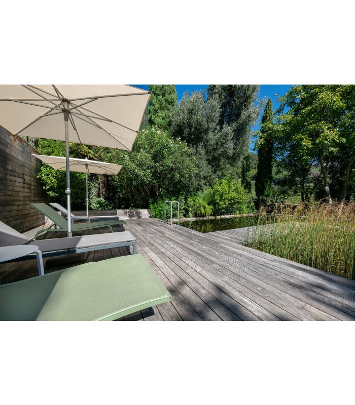 Grüne Liegestühle mit Naturbadeteich und beigem Schirm.