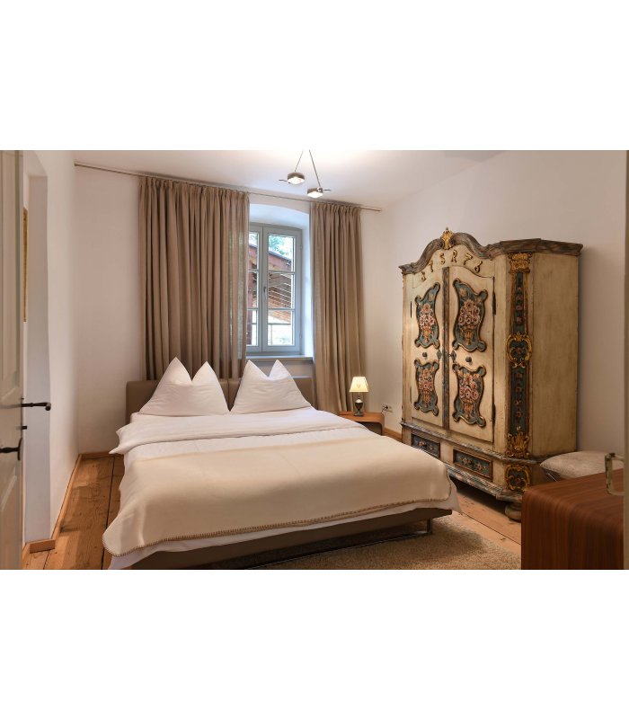Schlafzimmer mit Doppelbett und weißer Bettwäsche, daneben ein Schrank mit traditionellen Bemalungen
