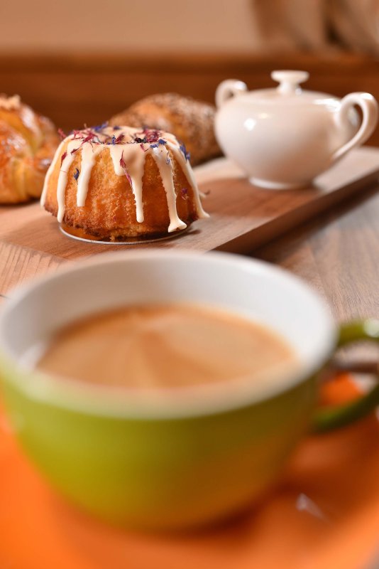Grüne Kaffeetasse mit frisch gebrühtem Kaffee, dahinter ein kunstvoll verzierter kleiner Gugelhupf
