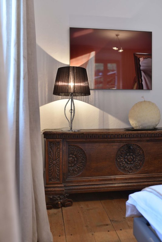 Holzkommode mit leuchtender Stehlampe darauf, dahinter ein großes rotes Kunstwerk an der Wand