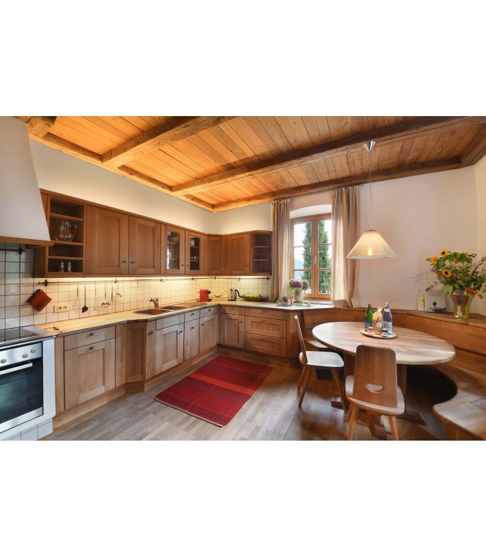 Küche mit großer Küchenzeile, rundem Holztisch, Holzdecke und kleinem roten Teppich auf dem Boden