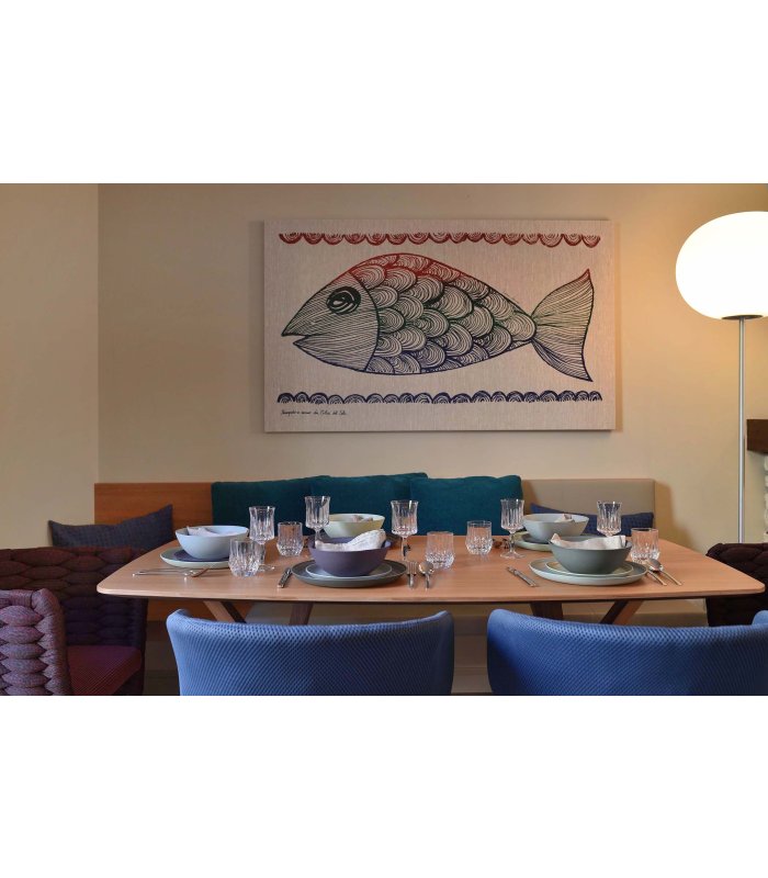 Gedeckter Tisch, blaue Stühle und dahinter ein Bild mit einem gemalten Fisch an der Wand