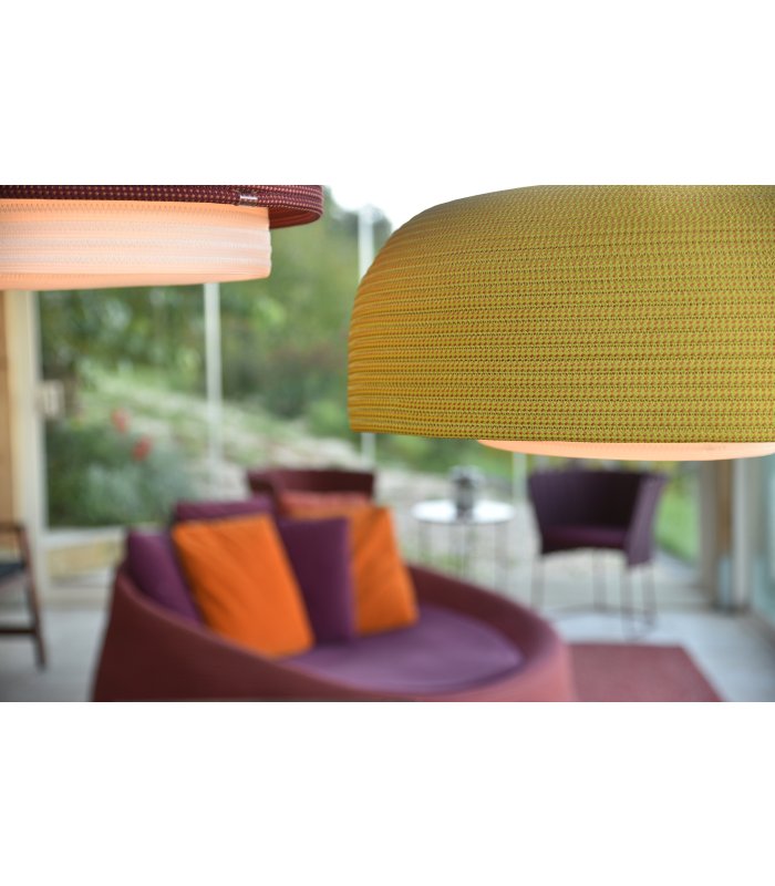 Grüne hängende Lampe im Vordergrund, im Hintergrund bunte Pölster und eine violette Couch