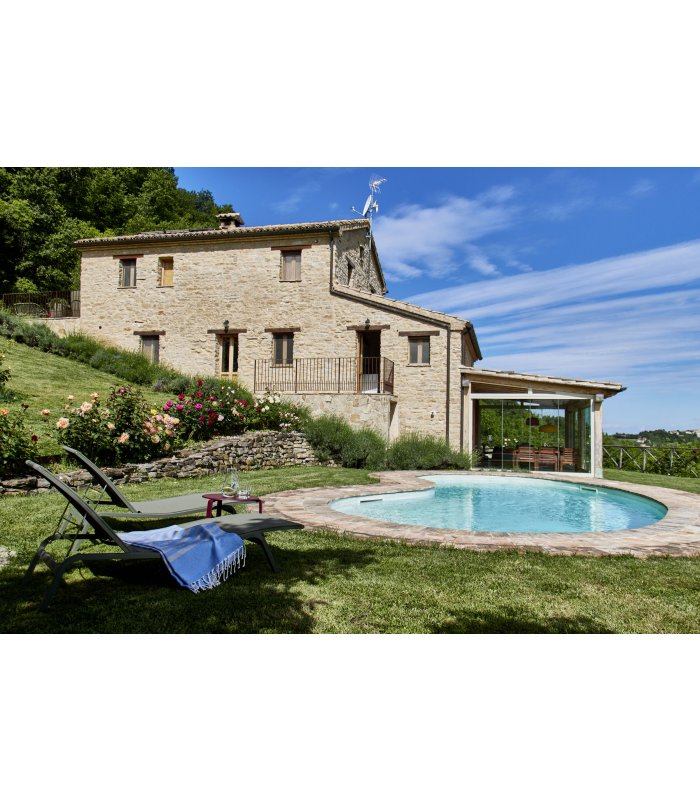 Natursteinhaus mit Pool, Liegestühlen und Garten unter blauem Himmel