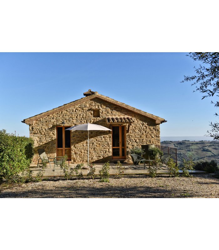 Natural stone house with a terrace and sun umbrella in a hilly landscape
