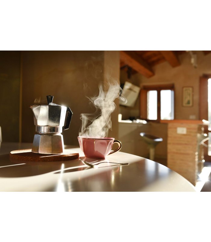 Dampfende Kaffeetasse und Espressokanne auf einem Holztisch in sonniger Küche