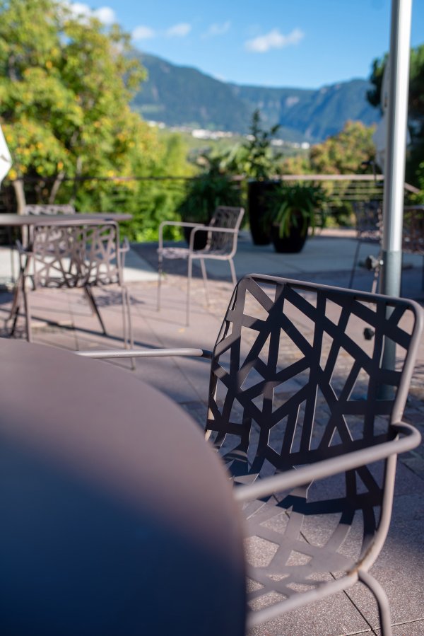 Gemütliche Terrasse mit Gartenmöbeln und Palmen in Algund an einem Sommertag.