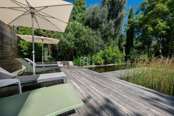 Grüne Liegestühle mit Naturbadeteich und beigem Schirm.