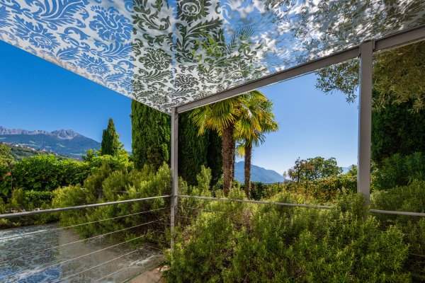Sonnige Terrasse in Algund mit Palmen unter klarem Himmel.