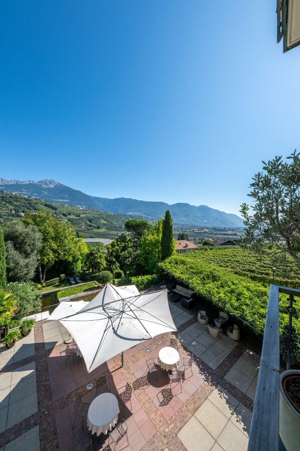 Sonnige Terrasse in Algund mit Palmen und hellen Stühlen unter klarem Himmel.