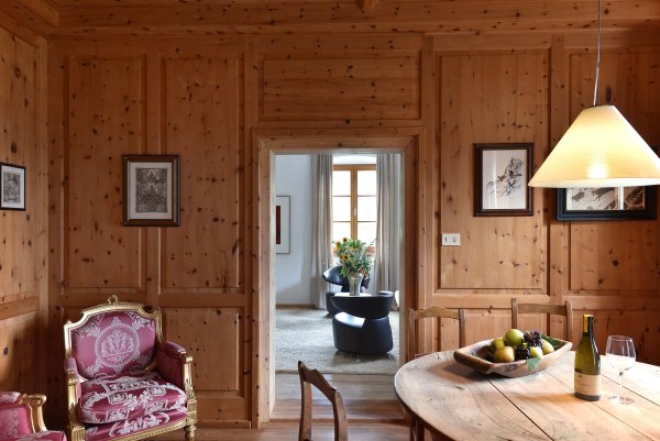 Stube mit Holztisch, edlen Holzvertäfelungen und üppigem lilafarbenem Ohrensessel in der Ecke