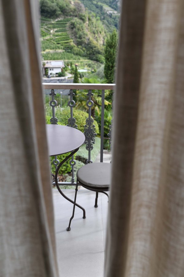 Blick zwischen dem grauen Vorhang durch auf den Balkon mit einem kleinen Tisch und Stühlen