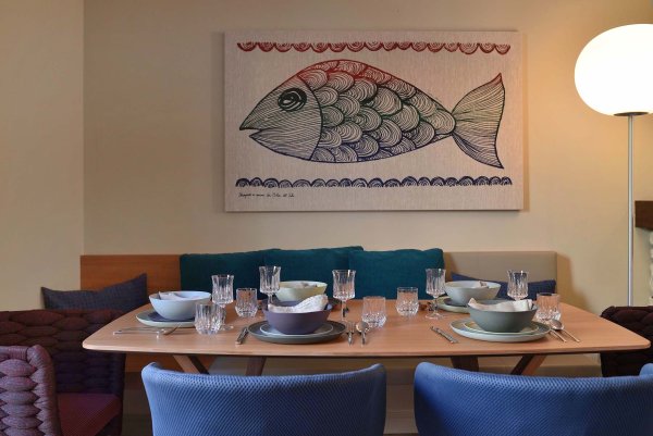 Gedeckter Tisch, blaue Stühle und dahinter ein Bild mit einem gemalten Fisch an der Wand