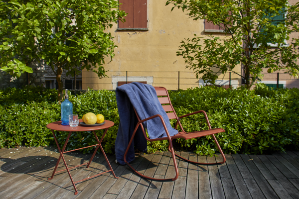 Ein roter Gartenstuhl auf einer Terrasse mit einem Handtuch und einem roten Beistelltisch mit einem Teller Zitronen