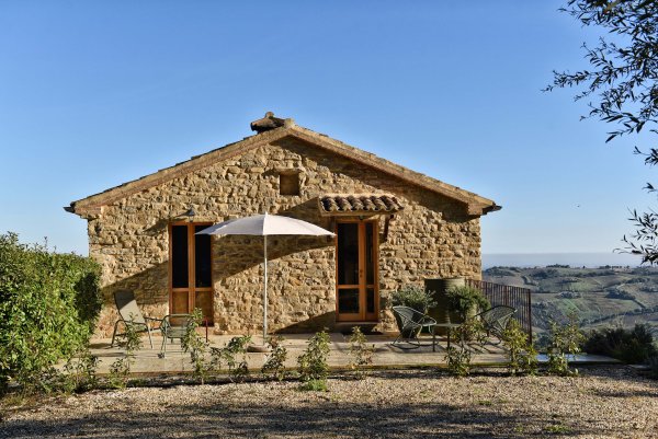 Natursteinhaus mit Terrasse und Sonnenschirm in hügeliger Landschaft