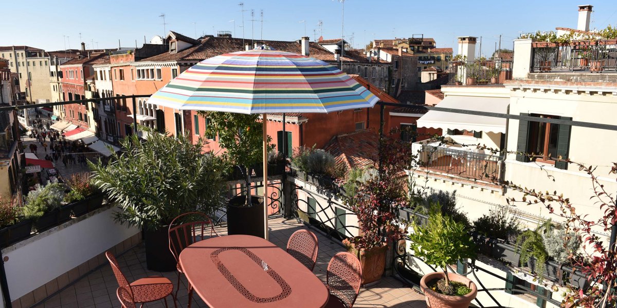 Eine sonnige Terrasse mit orangem Tisch und Stühlen mit Blick auf Venedig