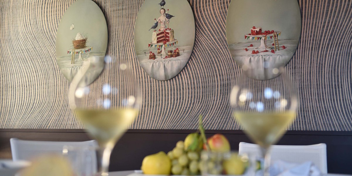 Bicchieri di vino pieni su tavola apparecchiata, sullo sfondo quadri rotondi sulla parete