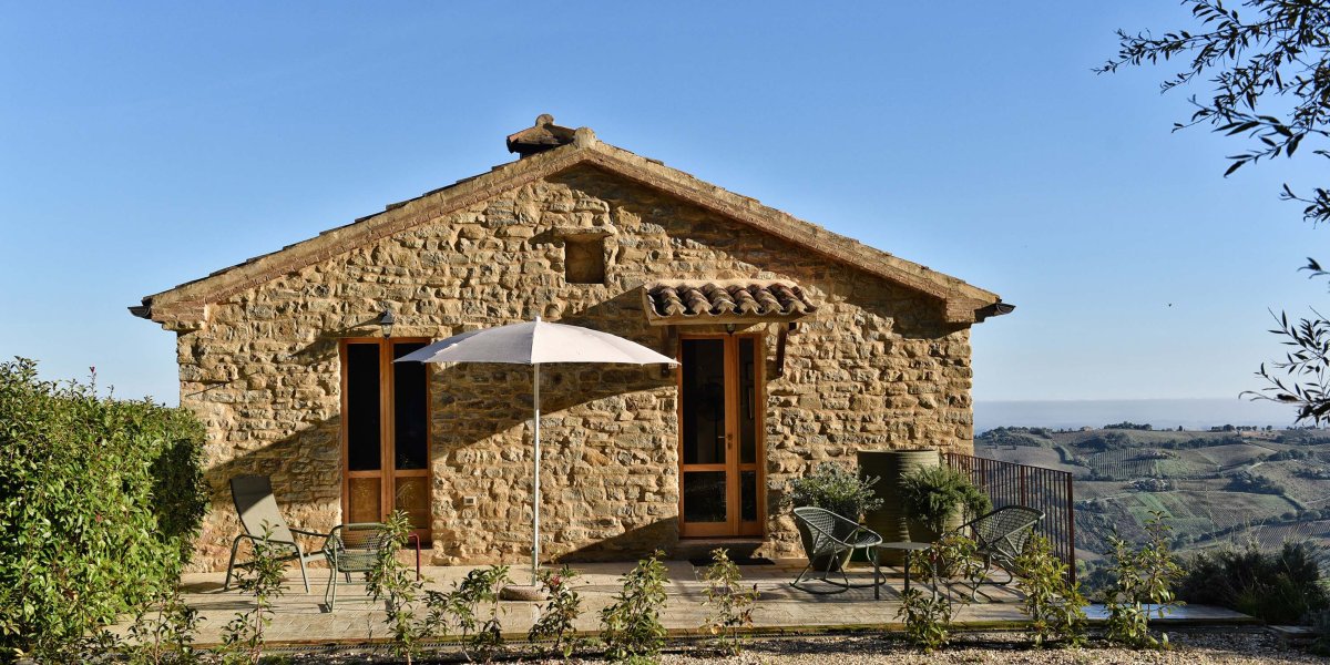 Natursteinhaus mit Terrasse und Sonnenschirm in hügeliger Landschaft
