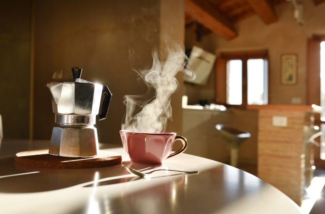 Bialetti-Kaffeemaschine, daneben eine braune Tasse mit dampfendem frischen Kaffee
