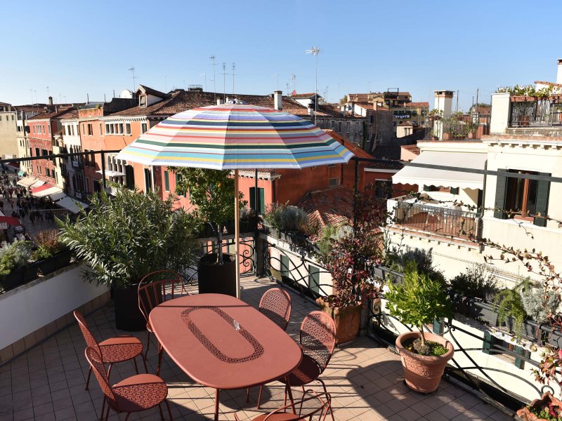 A sunny terrace with an orange table and chairs with a view of Venice