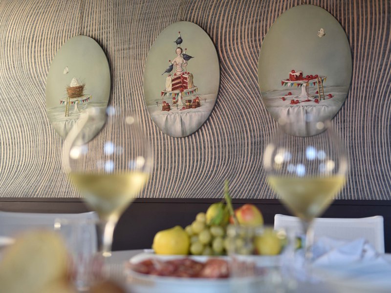 Bicchieri di vino pieni su tavola apparecchiata, sullo sfondo quadri rotondi sulla parete