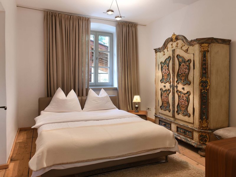 Schlafzimmer mit Doppelbett und weißer Bettwäsche, daneben ein Schrank mit traditionellen Bemalungen
