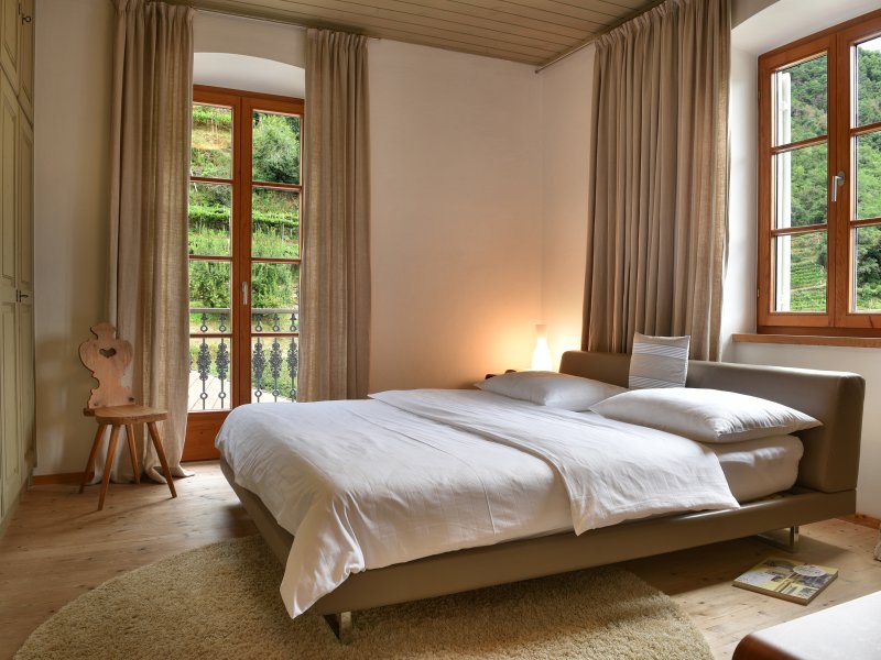 Letto accogliente con biancheria bianca davanti a grandi finestre con vista sul verde