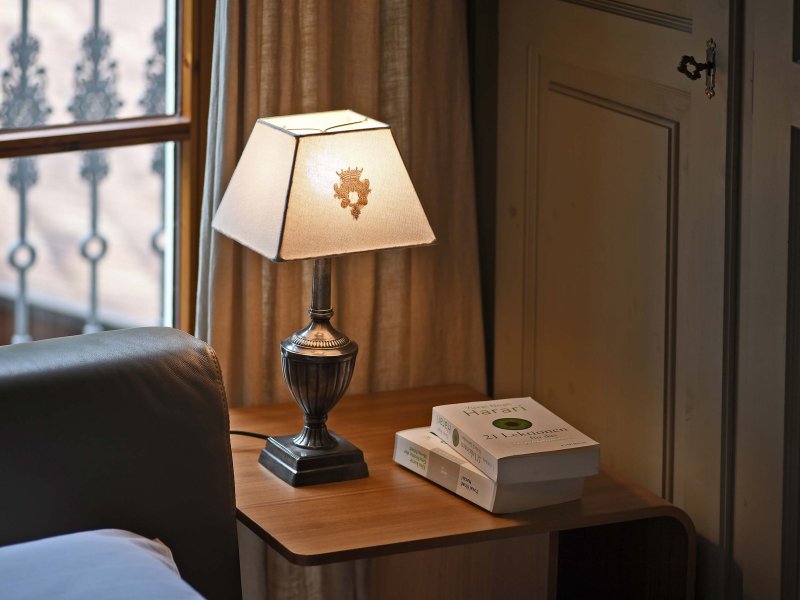 Holz-Beistelltisch neben grauer Couch, darauf eine kleine Lampe und drei gestapelte Bücher