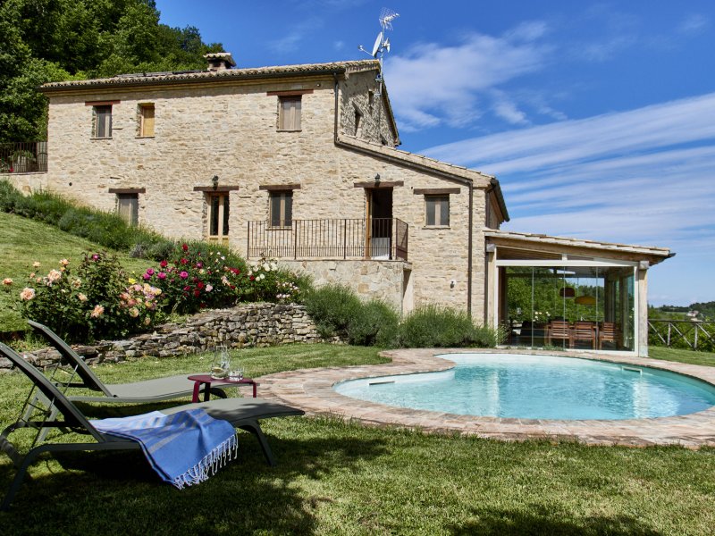 Casa in pietra con piscina, lettini e giardino sotto un cielo azzurro
