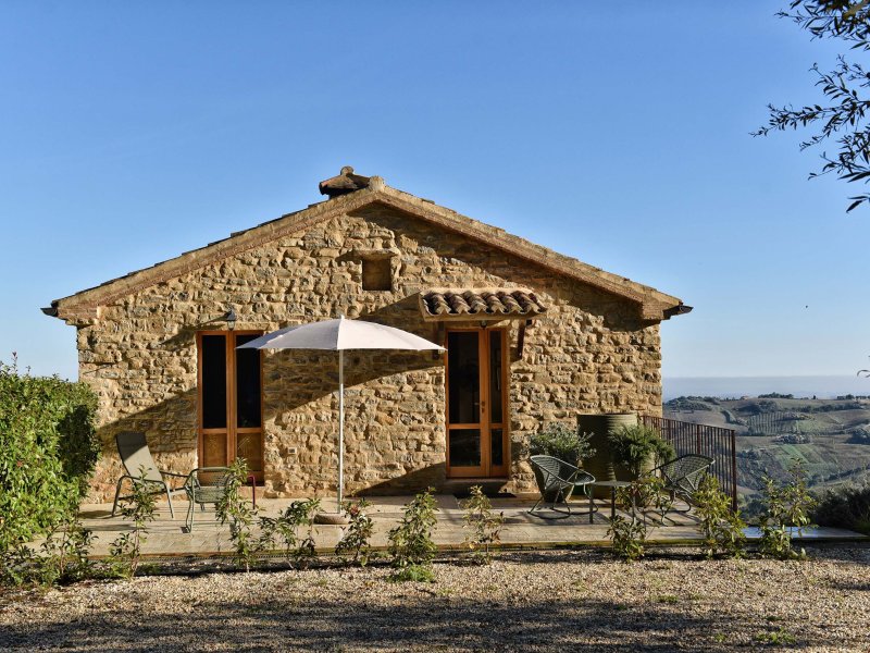 Natural stone house with a terrace and sun umbrella in a hilly landscape