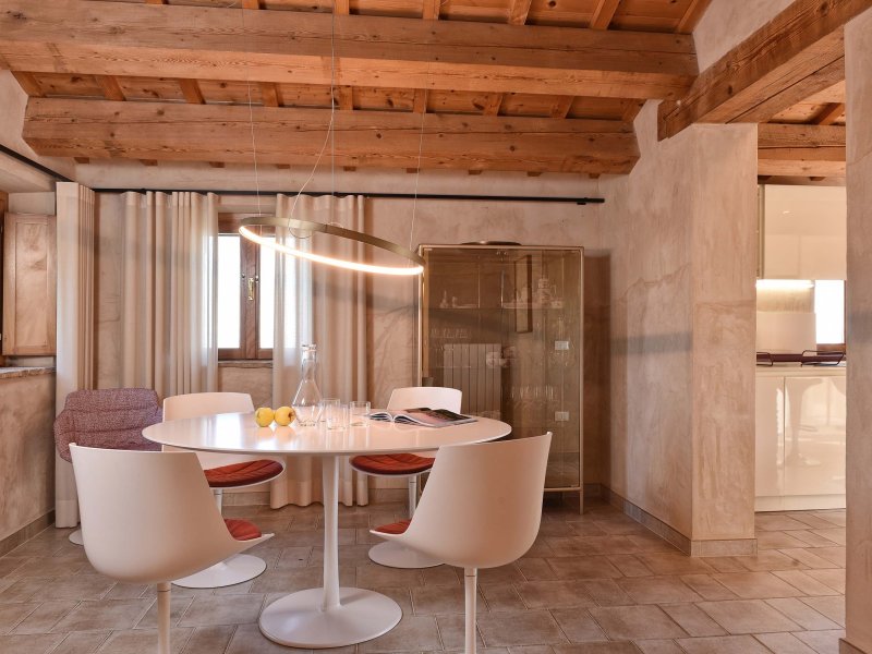 Accogliente zona pranzo con tavolo rotondo bianco e sedie moderne in una stanza con travi in legno